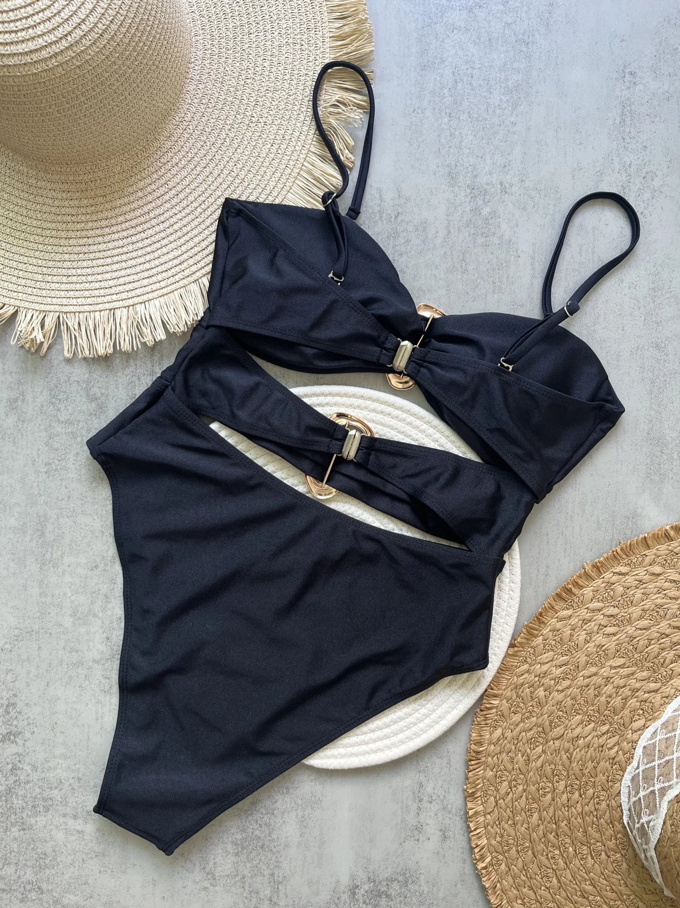 Navy blue bikini top with gold buckles on a gray surface with two straw hats.