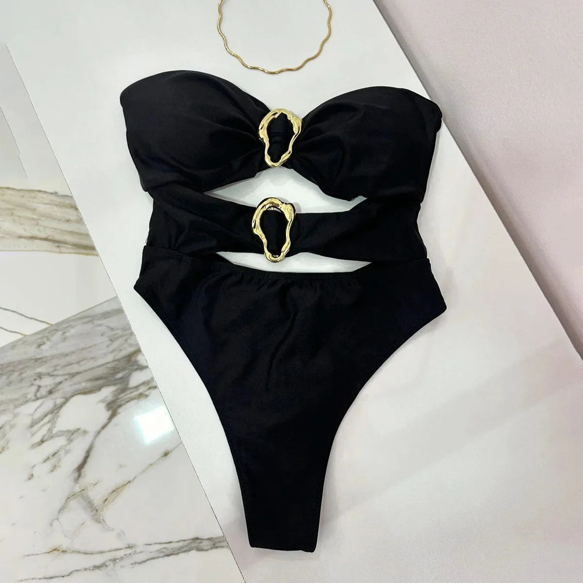 Black one piece with gold rings on a marble surface