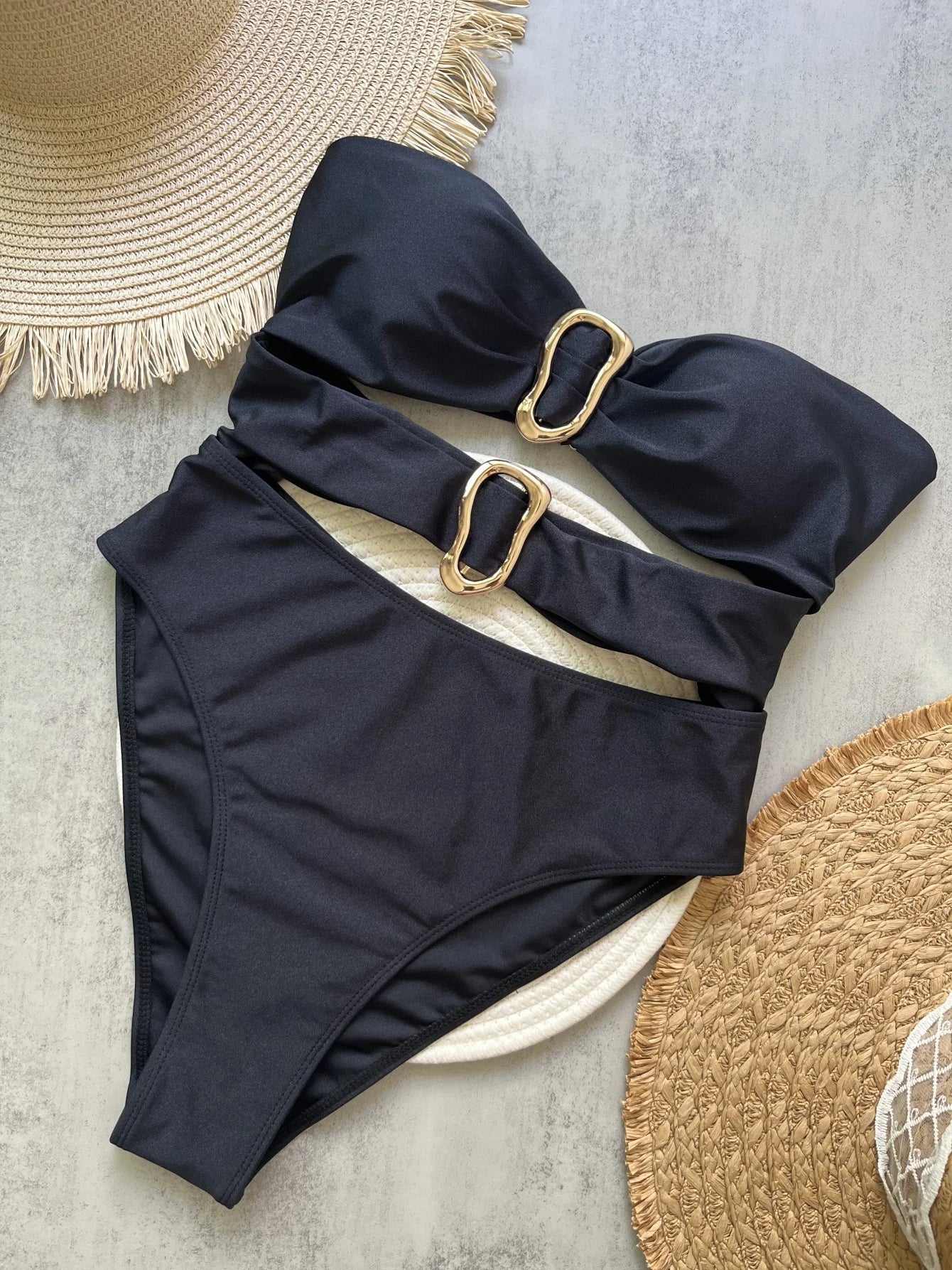 Black swimsuit with gold hardware on a textured surface with hats.