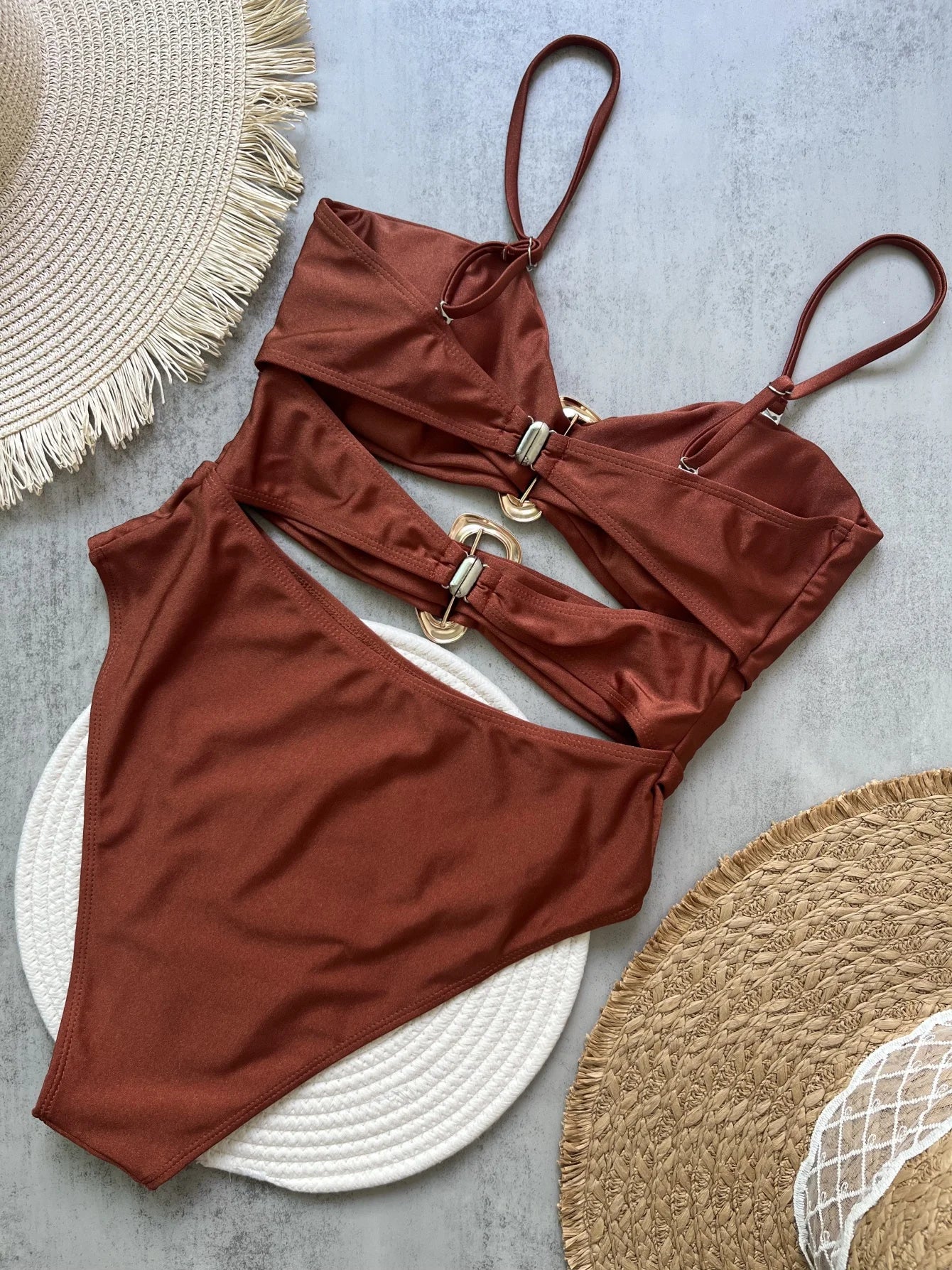 Brown bikini set on a textured surface with a hat and mat.