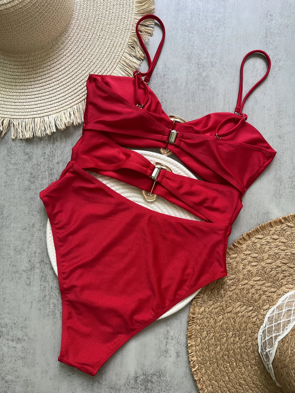 Red swimsuit with a belt and two straw hats on a gray surface