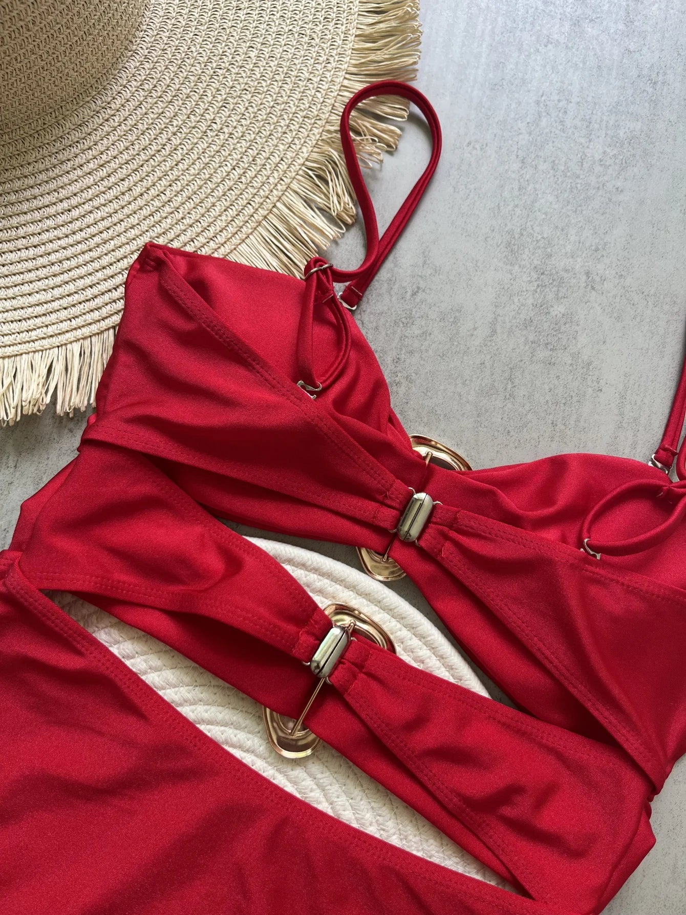 Red bikini with gold buckles on a textured surface with a straw hat.