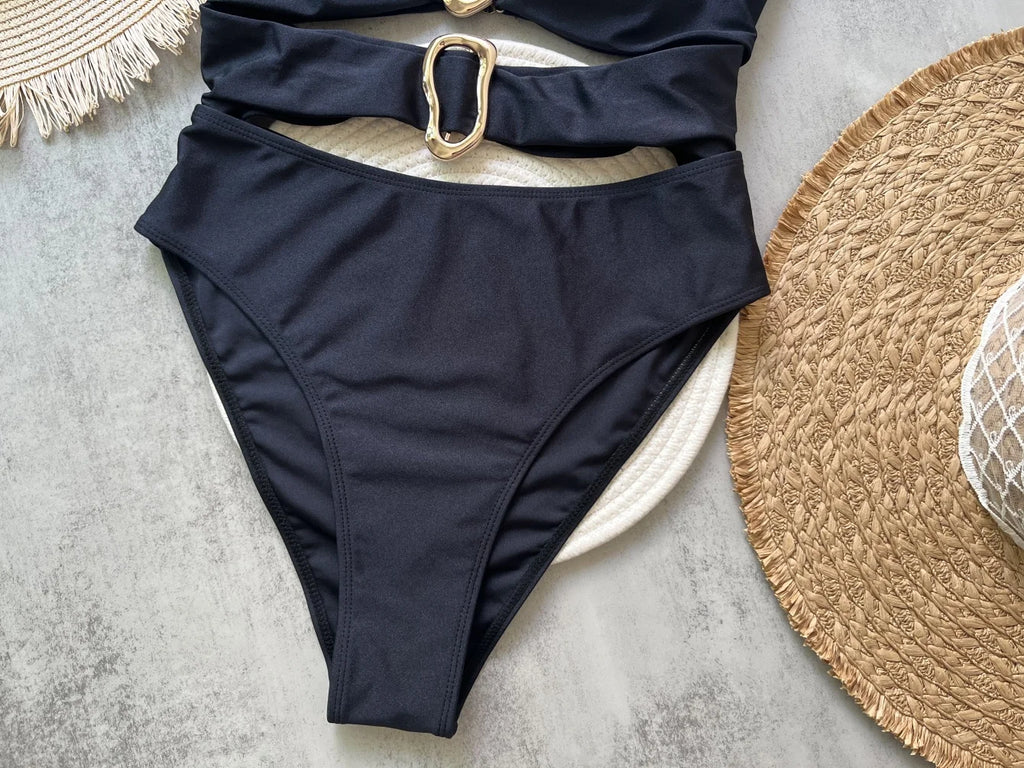 Black swimsuit with a gold buckle on a light gray surface with straw hats.