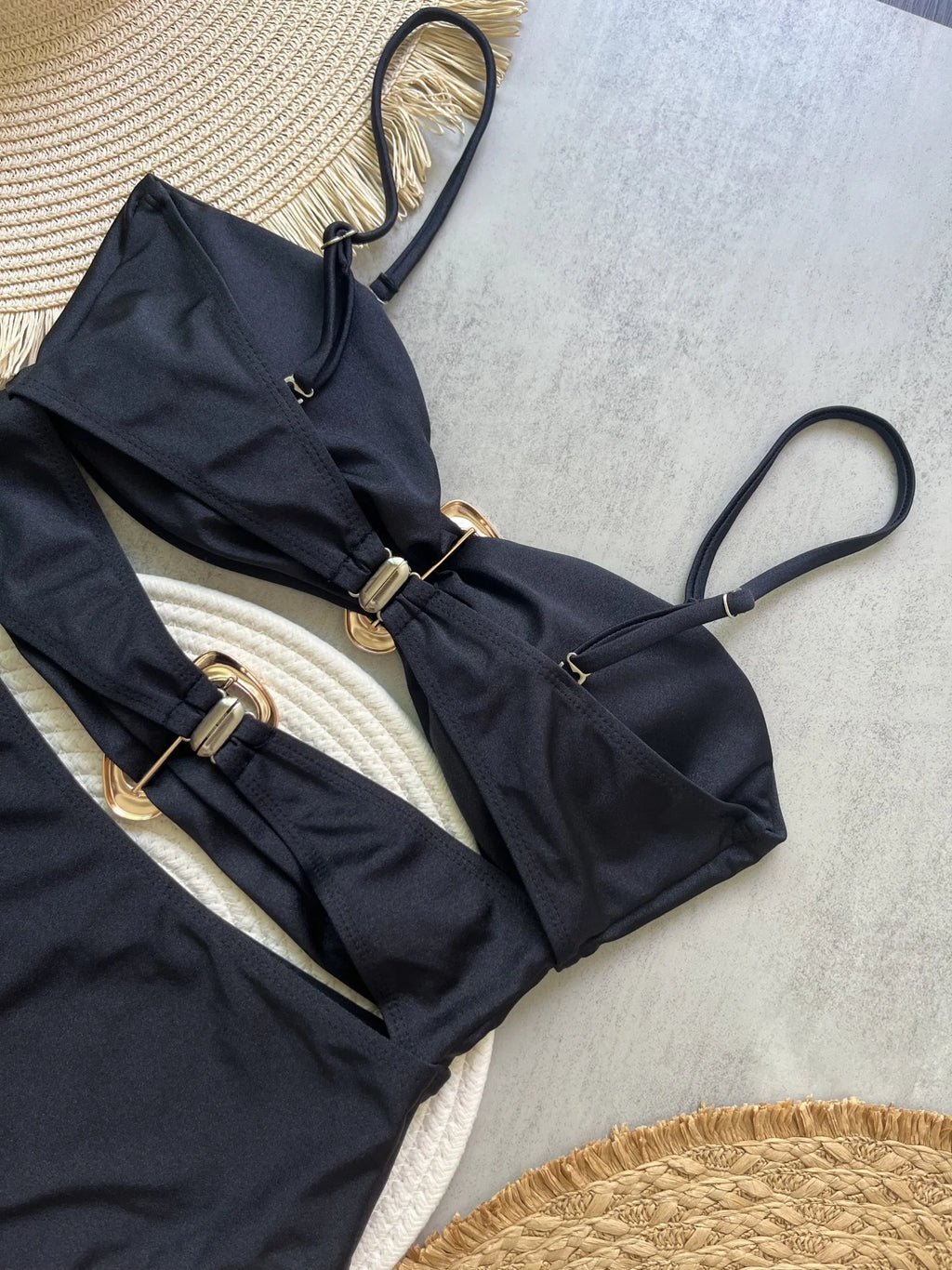 Black bikini top with gold buckles on a textured surface