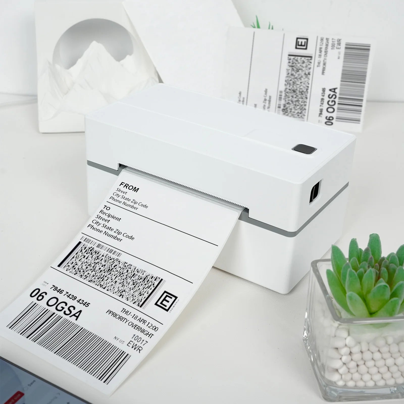 White label printer with printed labels on a white surface with a small plant.