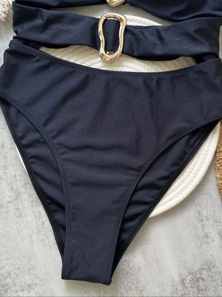 Black bikini bottom with a gold buckle on a textured surface